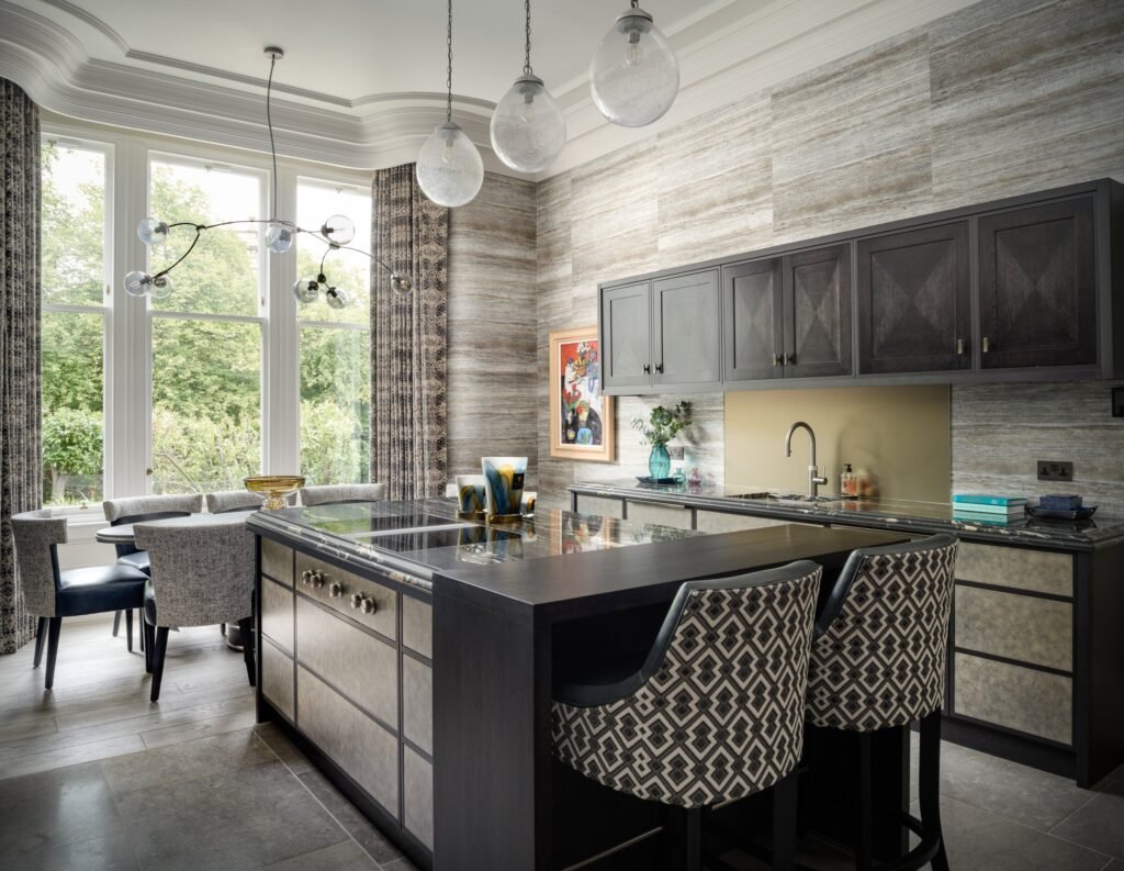 Contemporary kitchen with dark cabinets, textured wood-grain walls, marble island, patterned bar stools, and dining by windows.