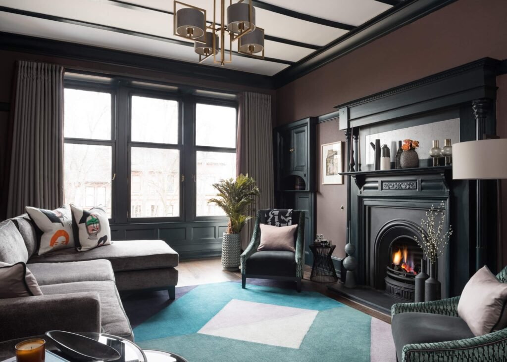 Moody, eclectic living room with deep brown walls, dark trim, a lit fireplace, grey sectional, and vibrant geometric rug.