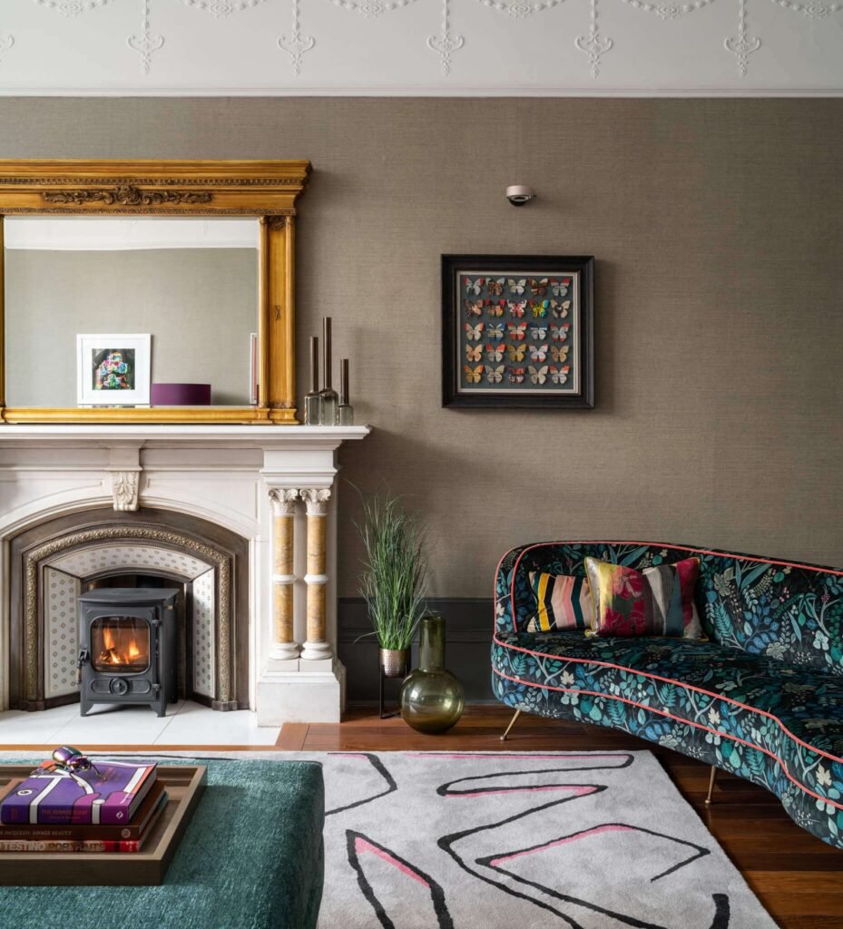 Eclectic living room with ornate fireplace, gold mirror, curved floral sofa, modern abstract rug, and butterfly art.