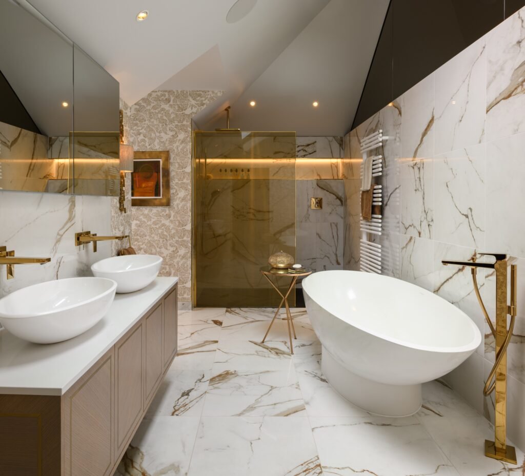 Opulent bathroom with white marble walls and floor, gold fixtures, freestanding tub, double vanity, and gold-toned glass shower.