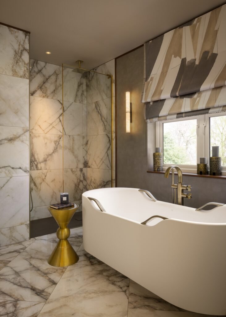 Luxurious bathroom with freestanding tub, marble shower and floor, brass fixtures, and a modern patterned Roman blind.
