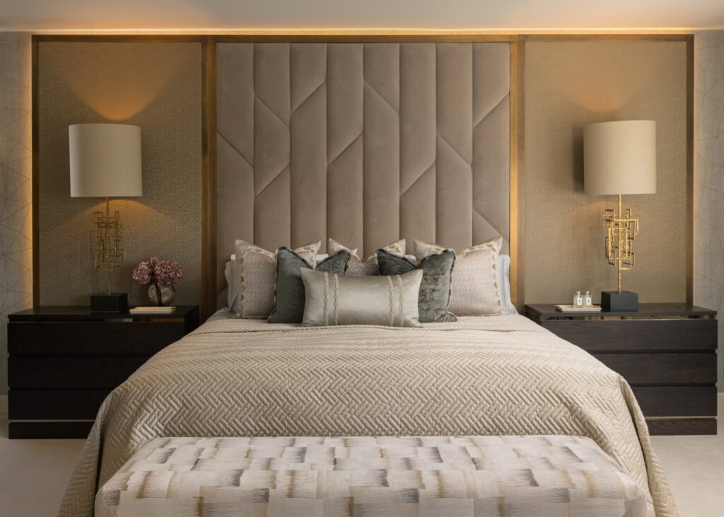 Luxurious modern bedroom with geometric upholstered headboard, elegant gold lamps, dark nightstands, and neutral bedding.