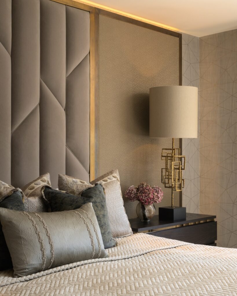 Modern luxury bedroom with geometric padded headboard, textured walls, gold sculptural lamp, and neutral bedding.