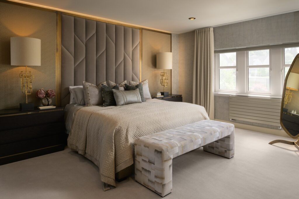 Modern luxurious bedroom with neutral tones, a striking geometric upholstered headboard, gold accents, and patterned bench.