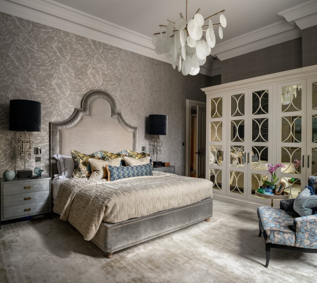 Luxurious modern bedroom with a grey upholstered bed, botanical wallpaper, statement chandelier, and mirrored wardrobe.
