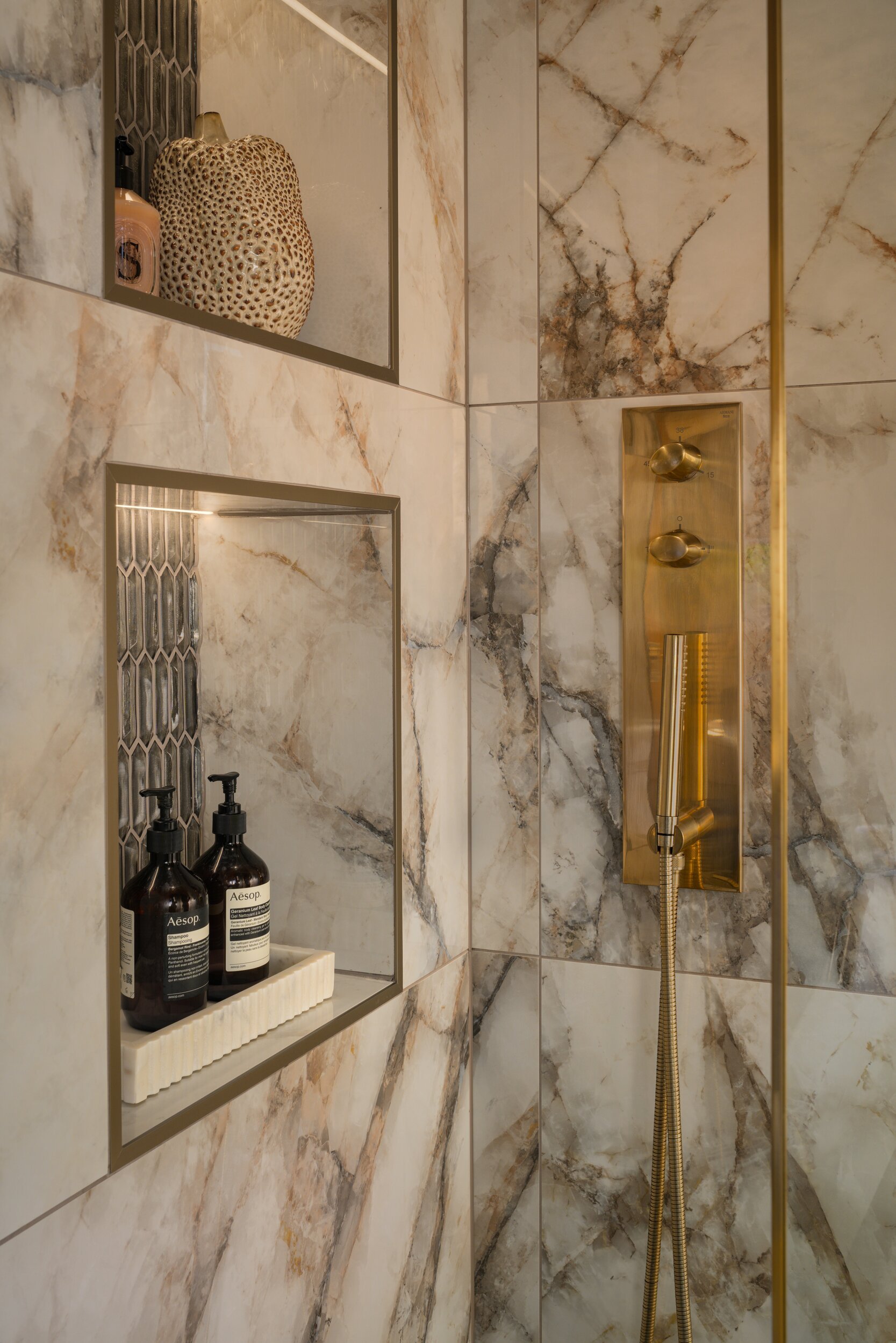 Luxurious shower with warm-toned marble tiles, brass shower controls, and two decorative recessed wall niches.