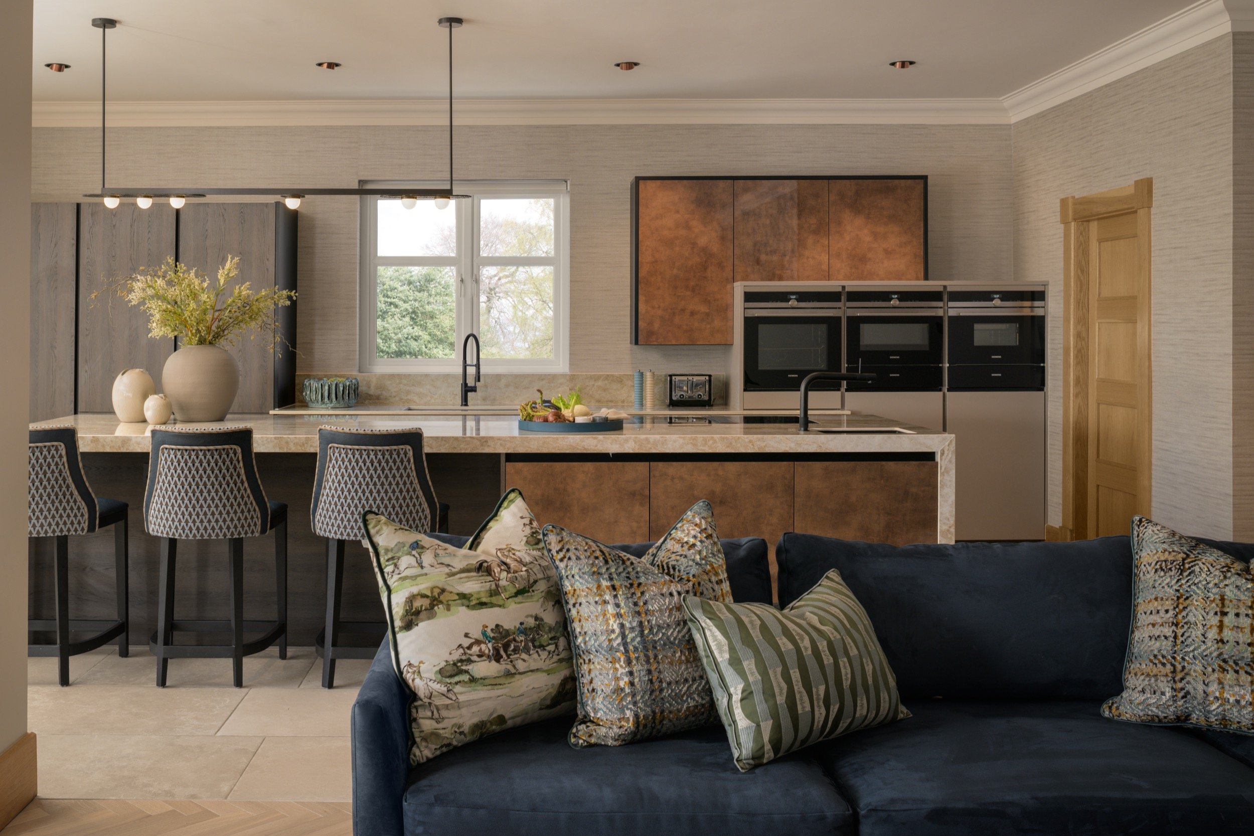 Luxury open-plan kitchen and living room with navy velvet sofa, textured cushions, bespoke copper cabinetry, and marble island.