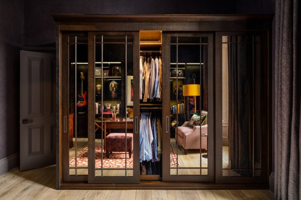 Sophisticated dark wood custom closet with sliding doors, revealing an illuminated study, lounge, and dressing area inside.