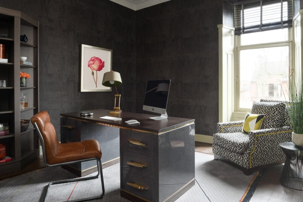 Modern dark grey home office with a sleek desk, brown leather chair, patterned armchair, bookshelf, and vibrant rose art.
