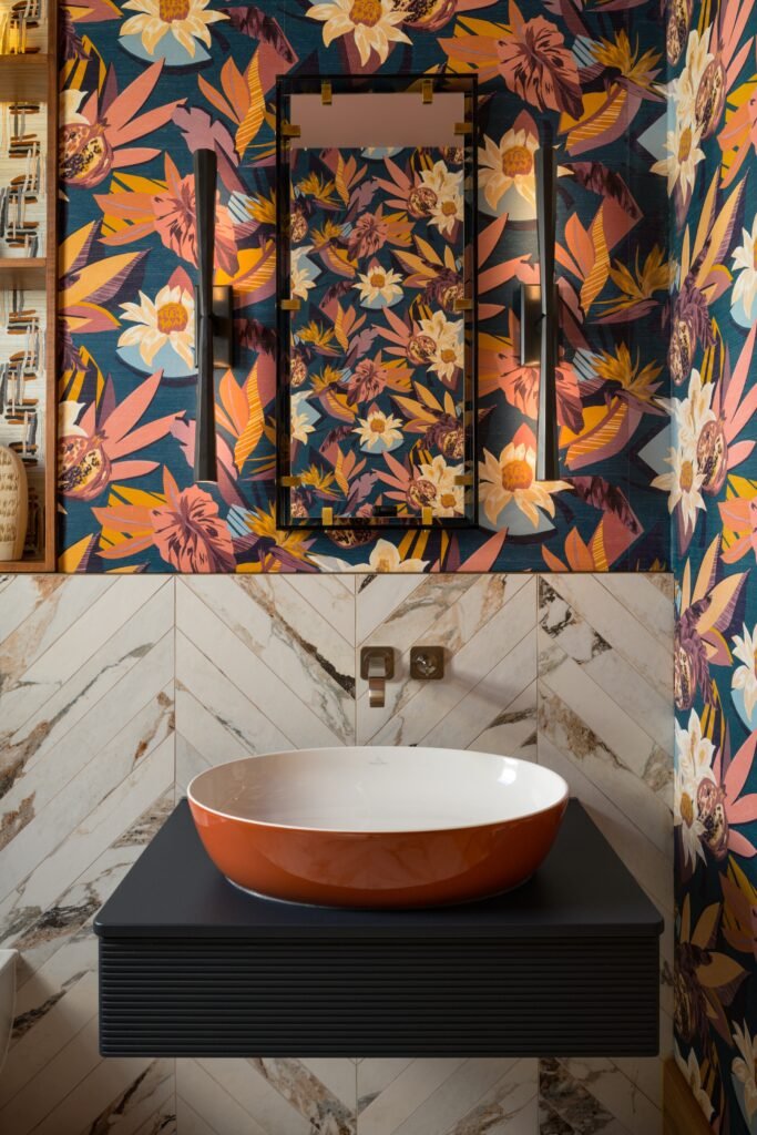 Vibrant tropical wallpaper bathroom with orange vessel sink, black floating vanity, and elegant herringbone marble backsplash.