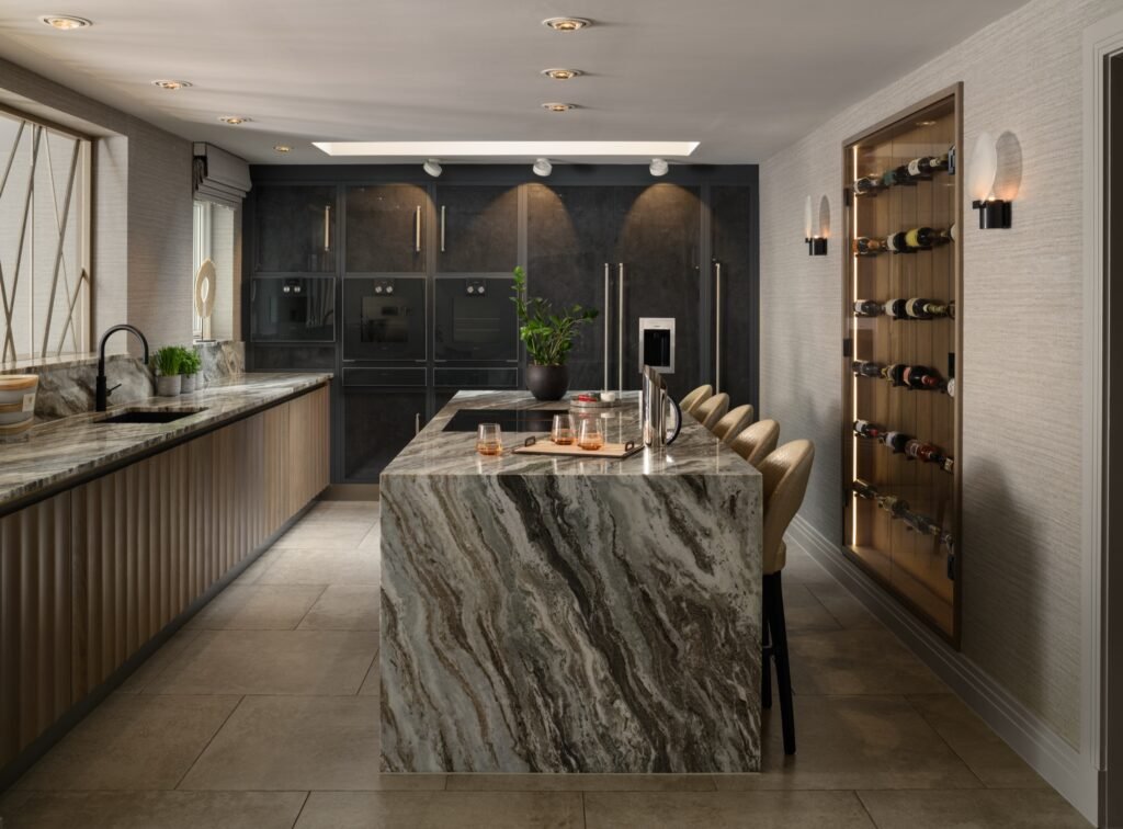 Luxurious, spacious kitchen with a large gray marbled island, wood slat cabinets, dark integrated appliances, and an illuminated wine display.