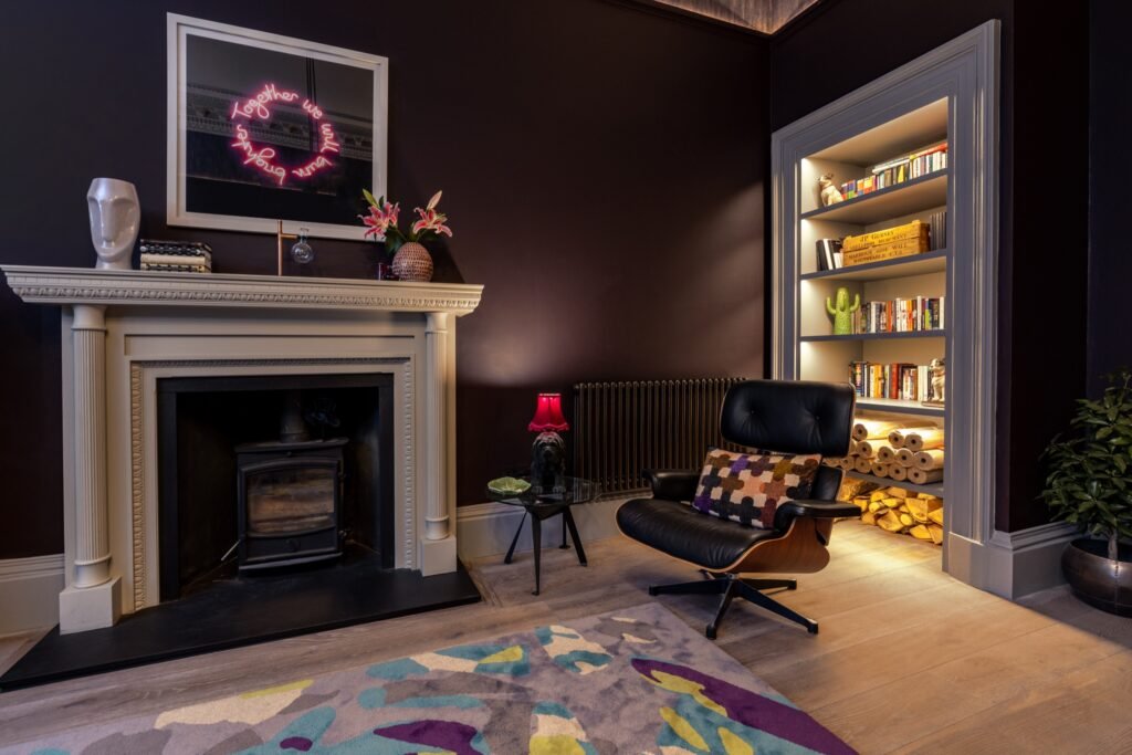 Modern eclectic living room: dark walls, white fireplace, 'Together we will bloom' neon, Eames chair, lit bookshelf, rug.
