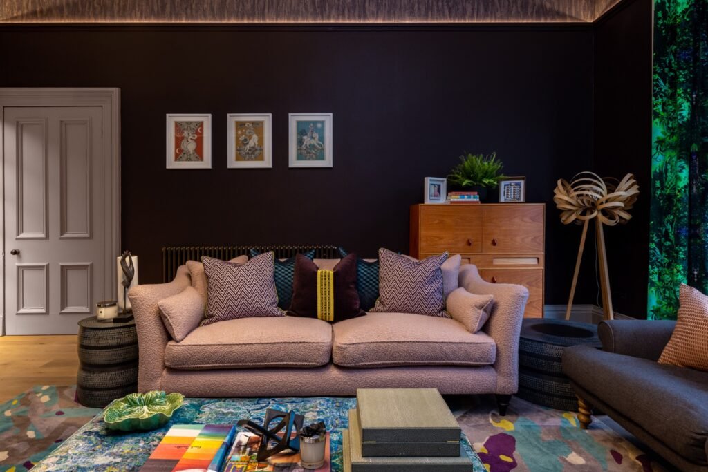 Pink boucle sofa in a vibrant living room with dark walls, eclectic art, colorful rug, and warm wooden accents.