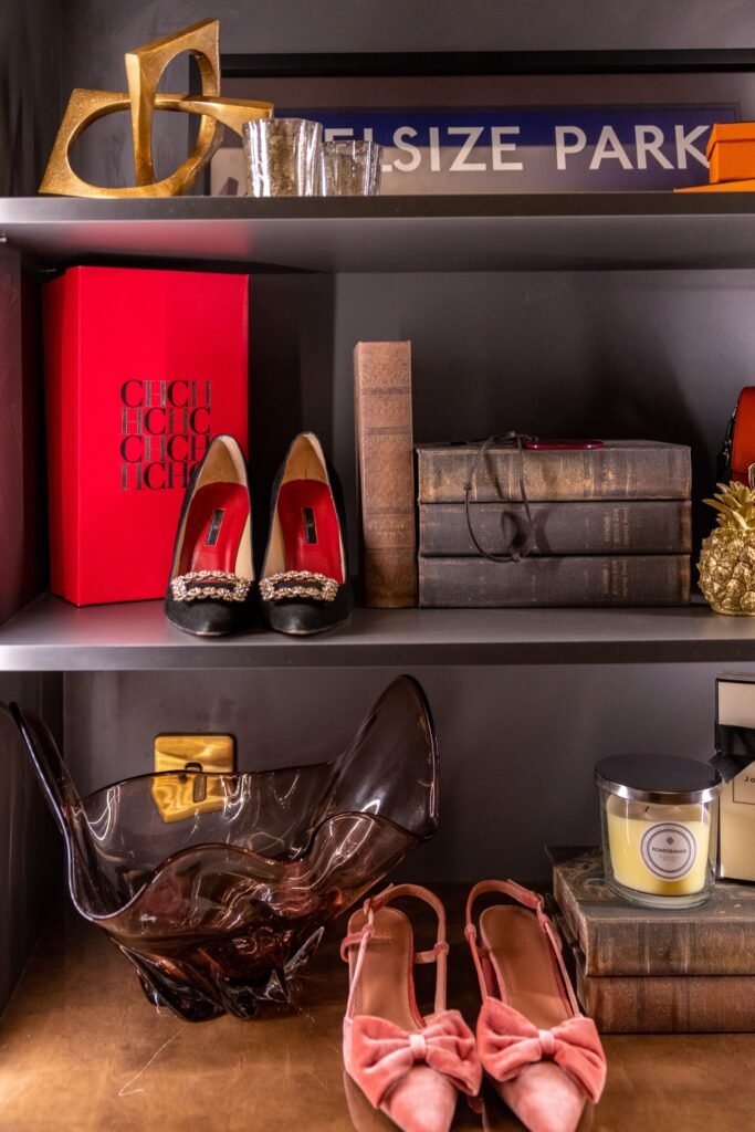 Elegant grey shelves with gold sculpture, luxury heels, vintage books, golden pineapple, amber bowl, and candle.