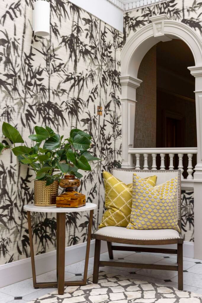 Chic entryway with black bamboo wallpaper, decorative white arch, gold plant pot, and a bench with yellow geometric pillows.