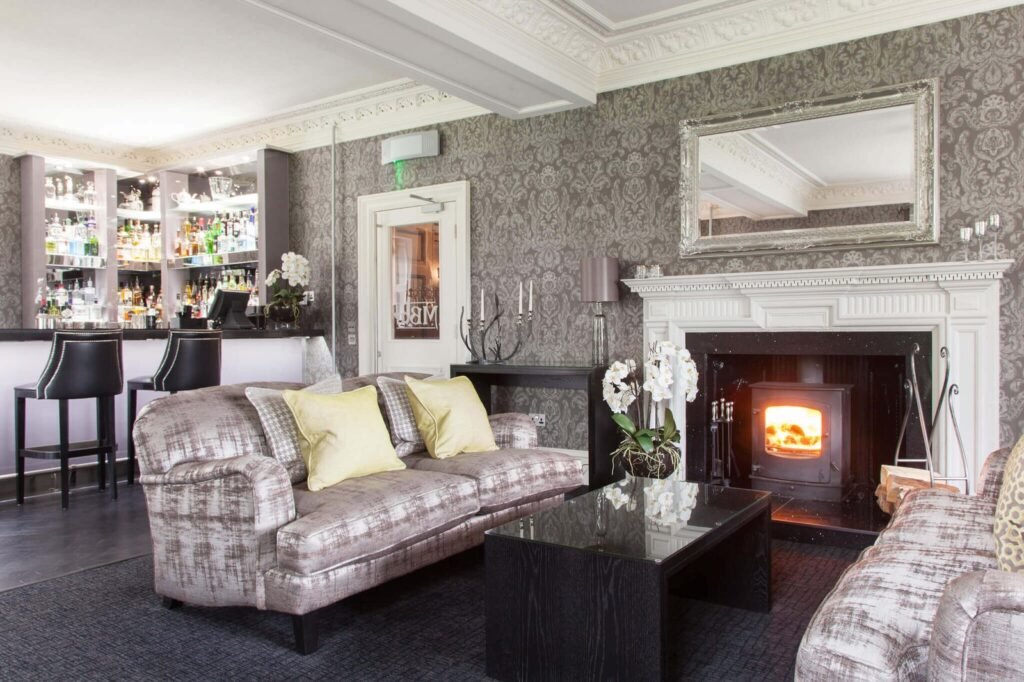 Plush hotel lounge bar with an ornate fireplace, patterned walls, comfortable sofas, and a well-stocked bar.