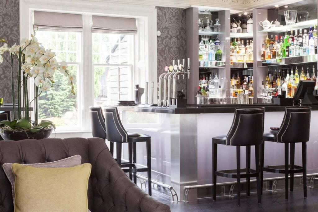 Elegant bar area with black studded stools, liquor display, beer taps, and lounge seating next to a window with orchids.