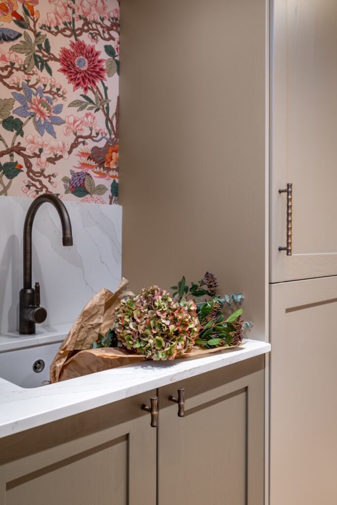 Eclectic design featuring vibrant floral wallpaper, bronze faucet, white quartz countertop, and a fresh hydrangea bouquet.
