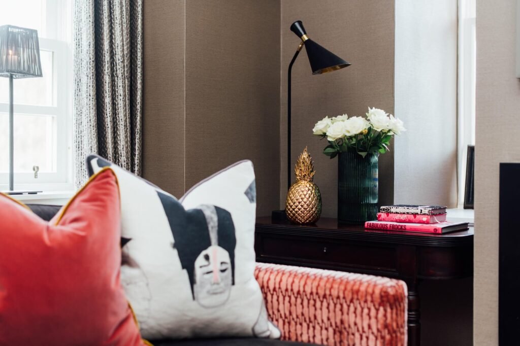 Stylish interior design featuring a graphic cushion, gold pineapple decor, white roses, and a black & gold table lamp.