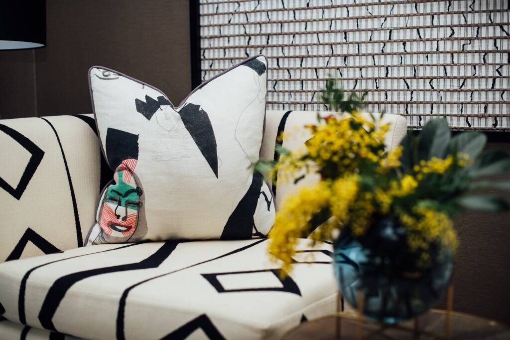 Stylish white and black geometric patterned sofa with an abstract art pillow featuring a colorful face and yellow flowers.