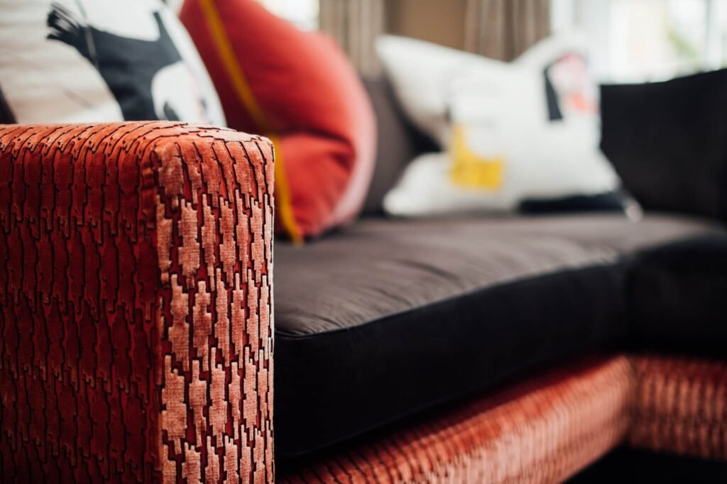 Close-up of a rust-orange textured sofa arm with a geometric pattern, part of a dark sectional with accent pillows.