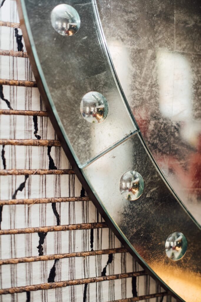 Close-up of a large round antiqued mirror with reflective glass buttons, next to a striped wall covering with natural fibers.