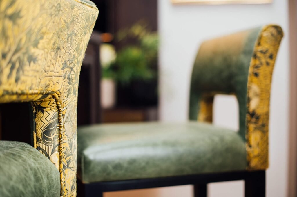 Elegant chairs with intricate yellow botanical patterned fabric and distressed green leather seats.