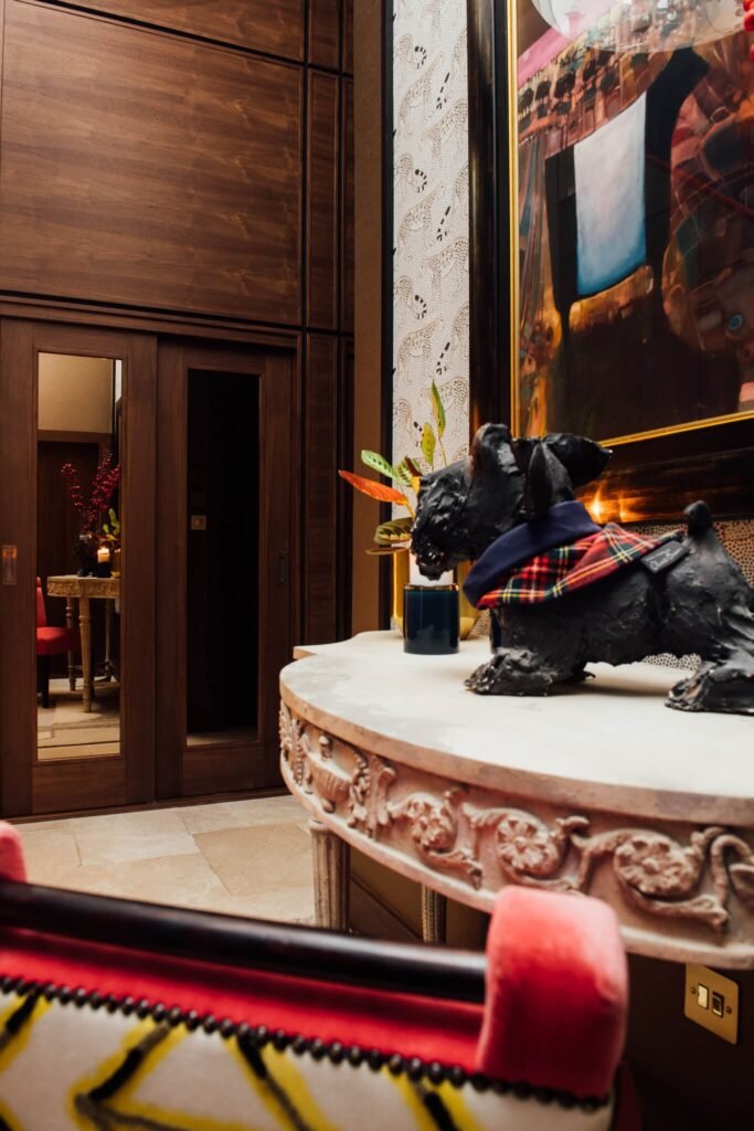 Luxurious eclectic interior: black dog sculpture on an ornate console, leopard wallpaper, abstract art, and dark wood doors.