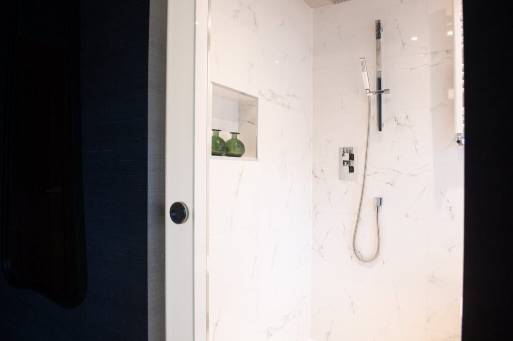 Modern shower interior with white marble-look tiles, chrome fixtures, and a niche with two green decorative bottles.