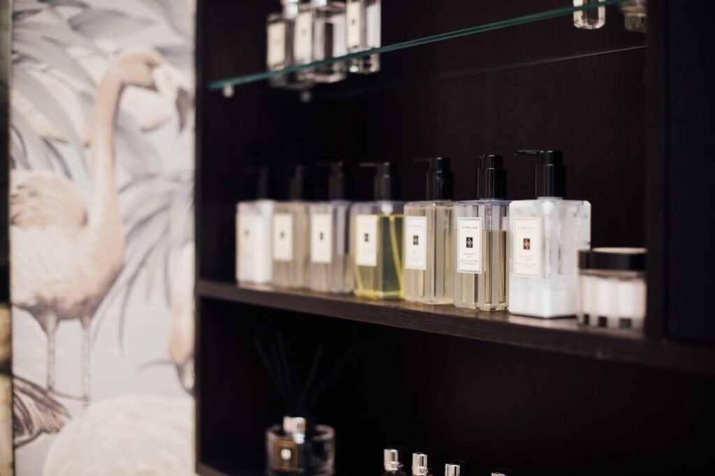 Elegant Jo Malone products on dark shelves next to a blurred flamingo wallpaper.