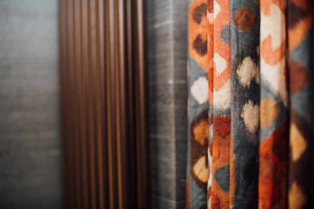 Ikat-patterned curtains (orange, blue, brown) with dark textured fabric and slatted wood paneling, showcasing interior design materials.
