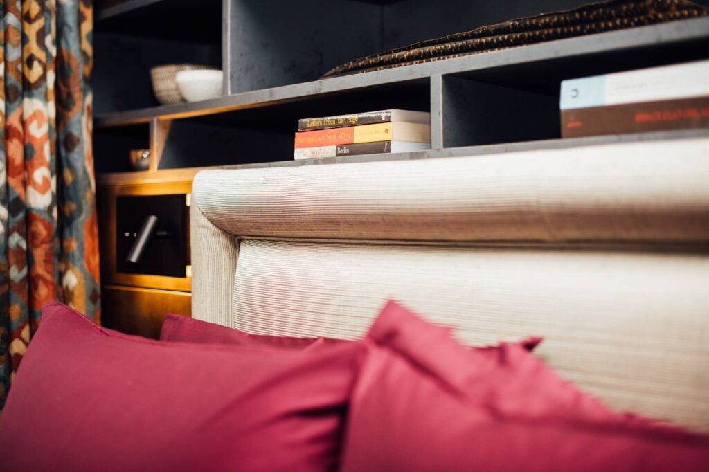 Modern bedroom with magenta pillows on a textured headboard, vibrant patterned curtain, and dark built-in shelves with books.