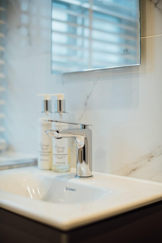 Modern bathroom vanity with white sink, chrome faucet, hand soap, and marble backsplash.