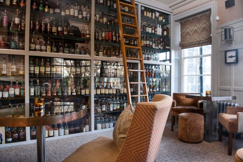 Sophisticated bar lounge with floor-to-ceiling glass cabinets filled with whisky bottles, a rolling ladder, and cozy armchairs.