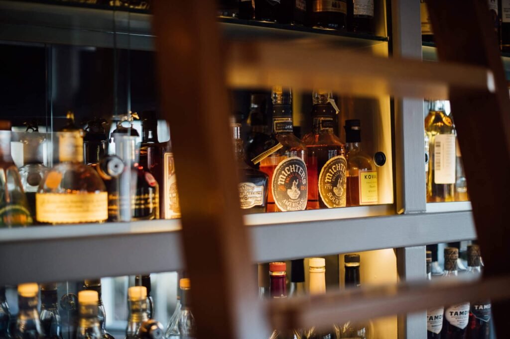 Illuminated bar shelves filled with Michter's bourbon and other whiskey bottles, with a wooden ladder in the foreground.