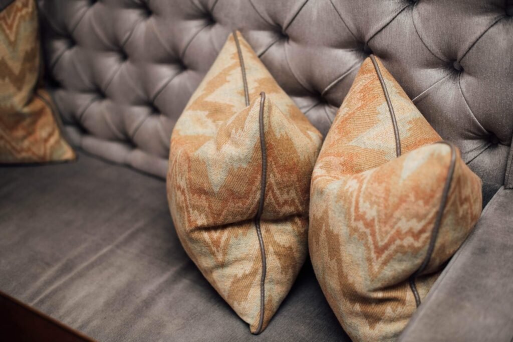 Close-up of a grey tufted sofa with orange and beige zigzag patterned throw pillows.