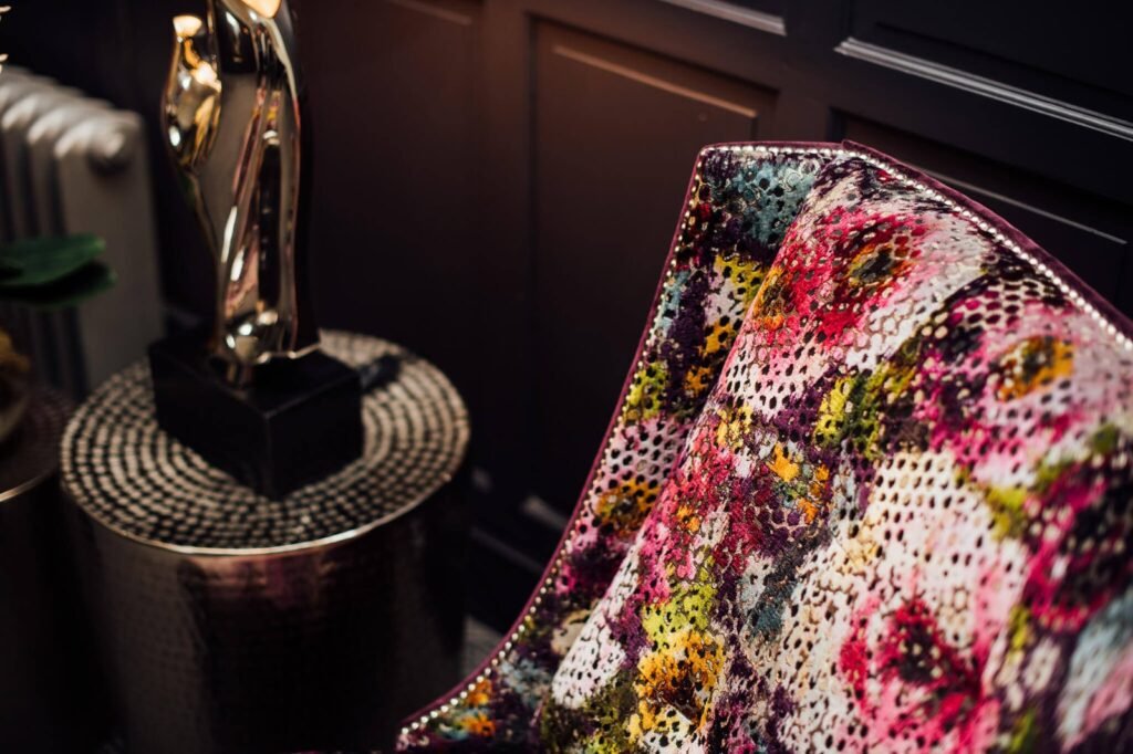 Vibrant, multicolor abstract perforated upholstery on an armchair with studded trim, next to a gold sculpture in a dark paneled room.