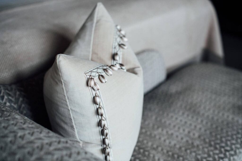 Cream decorative pillows with unique beaded trim on a textured gray bedspread.