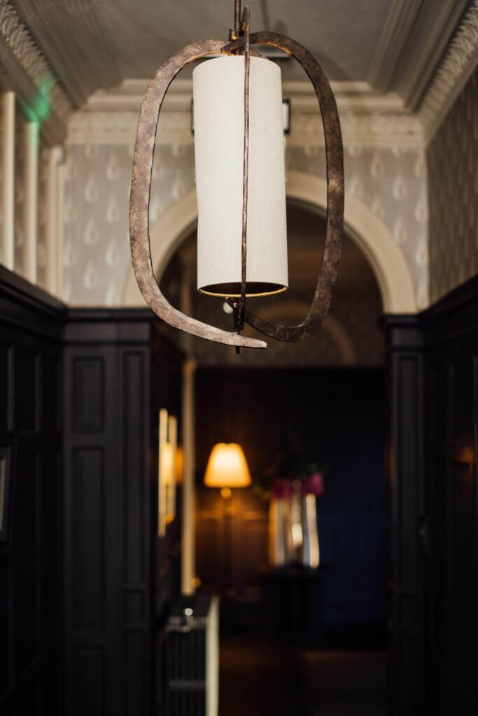 Elegant hallway with a prominent rustic iron chandelier, dark wood paneling, decorative wallpaper, and inviting warm light.
