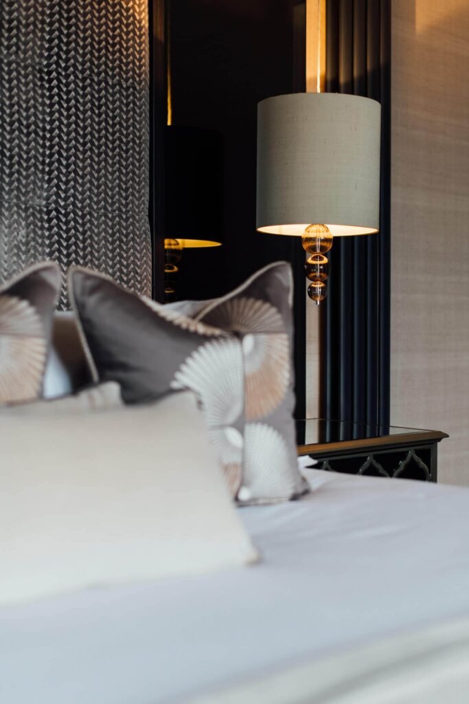 Elegant bedroom interior with patterned pillows, a decorative bedside lamp, and textured walls.